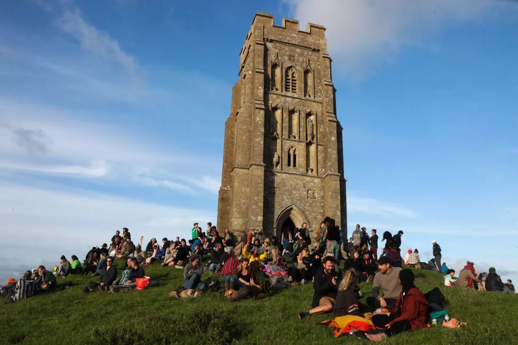 A crowd of people at Glastonbury Tor having picnics on a sunny day.